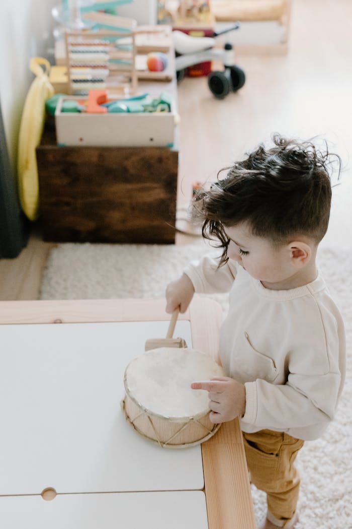 A young child playing with a drum in a brightly lit playroom, surrounded by toys.