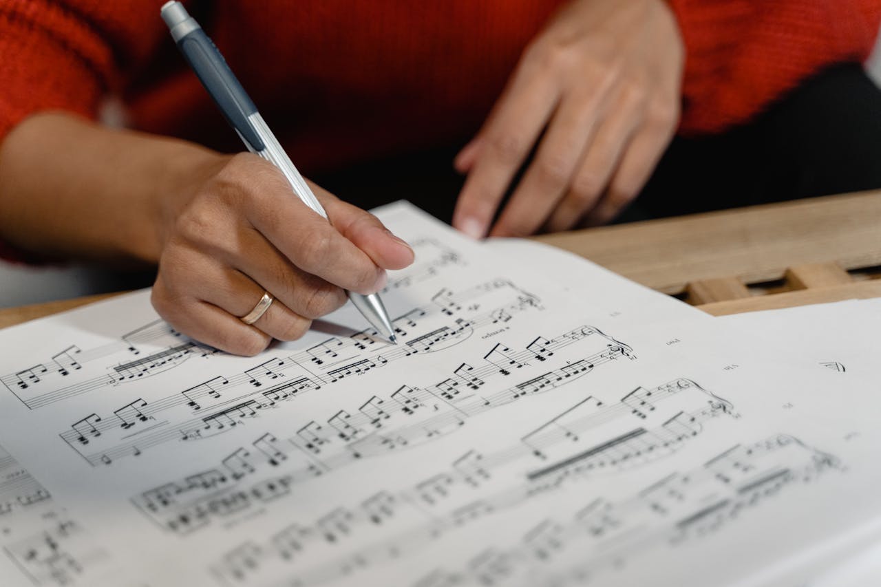 A person writes on sheet music with a pen, focusing on musical notation.