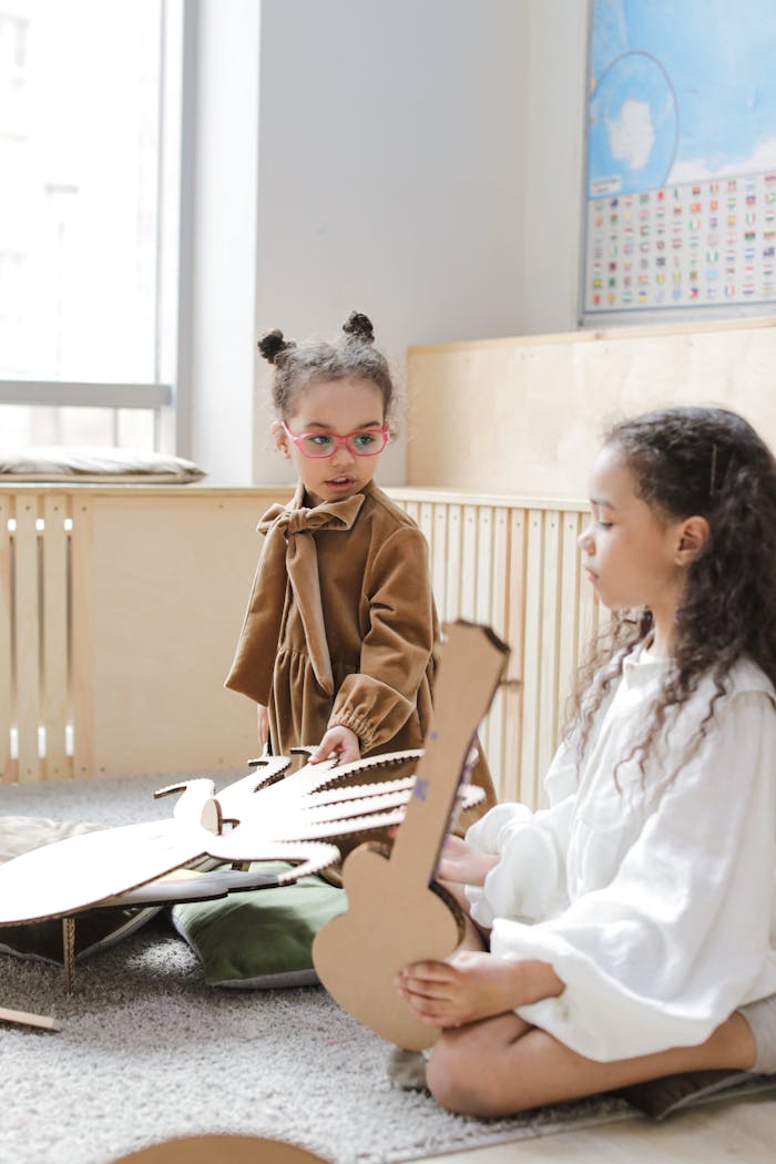 Two young girls engaged with cardboard guitar cutouts in a bright classroom setting.